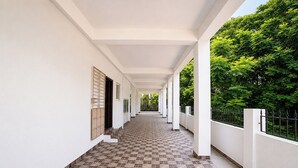 A covered corridor with tiled flooring, white walls, and a view of greenery.