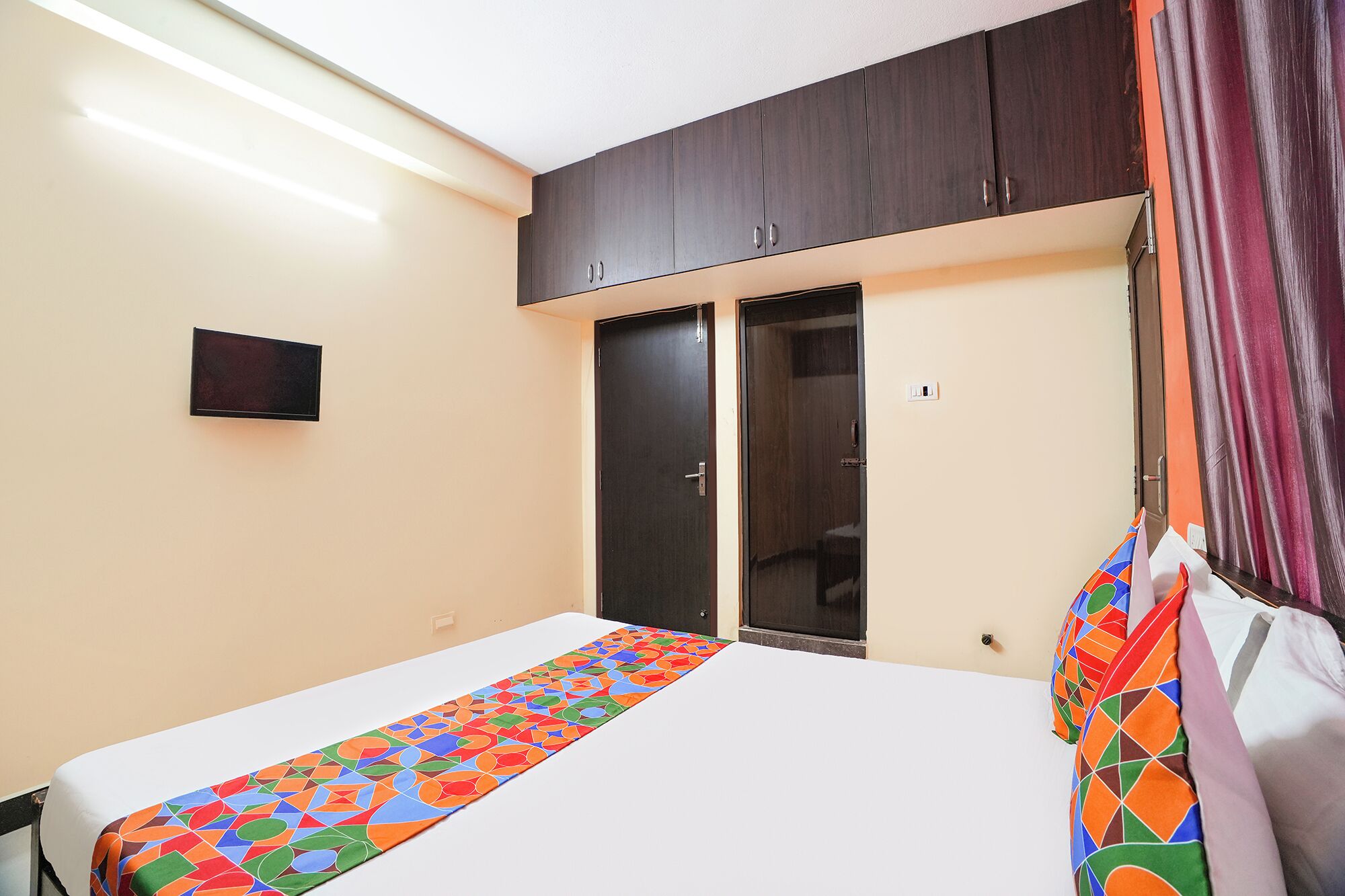 Quarto com cama, guarda-roupa, televisão e cortina.