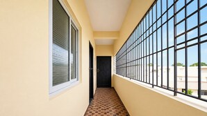 A corridor with tiled flooring, large windows with metal bars, and a door at the end.