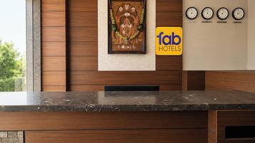 Un comptoir d’accueil d’hôtel avec un plateau en marbre, un mur revêtu de panneaux en bois, une œuvre d’art encadrée, des horloges indiquant différents fuseaux horaires et un panneau indiquant « fab hotels ».