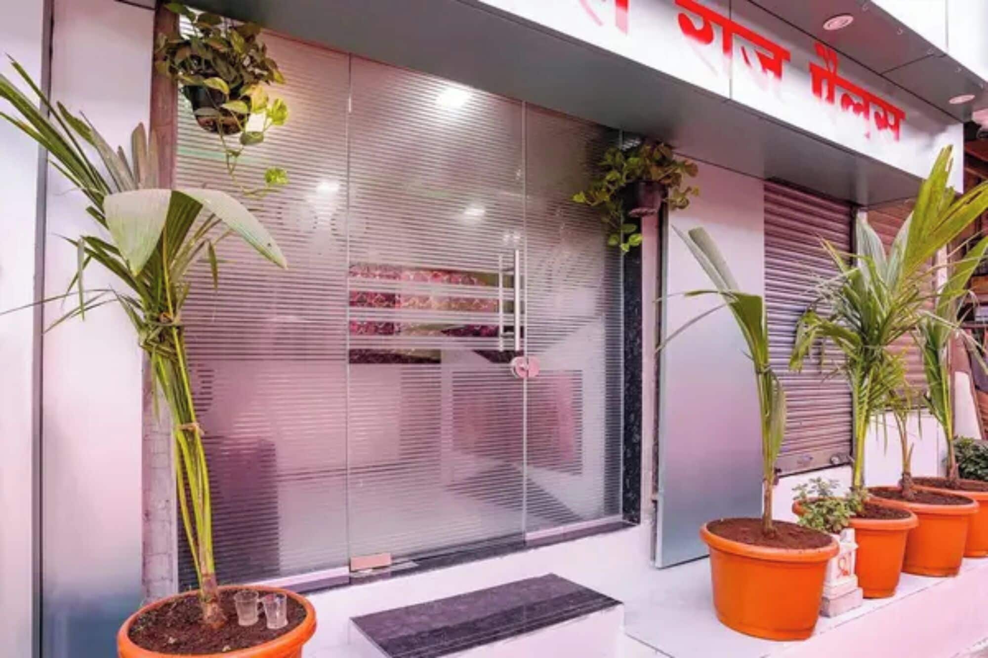 A building with a closed shutter, potted plants, and a sign with red text.