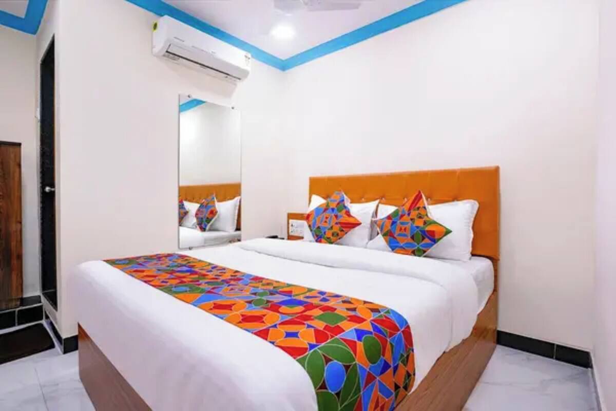 A hotel room with a bed, a mirror, and an air conditioning unit.