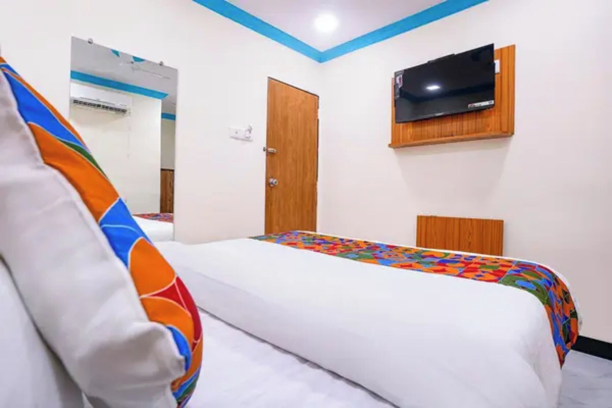 Una habitación de hotel con una cama, un televisor montado en la pared y una puerta.