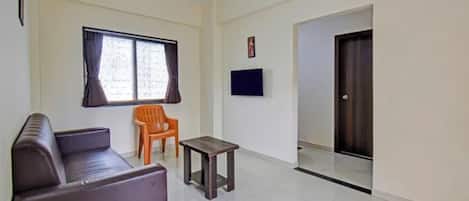 Una sala de estar con un sofá, una mesita, una silla, un televisor y una puerta que da a otra habitación.
