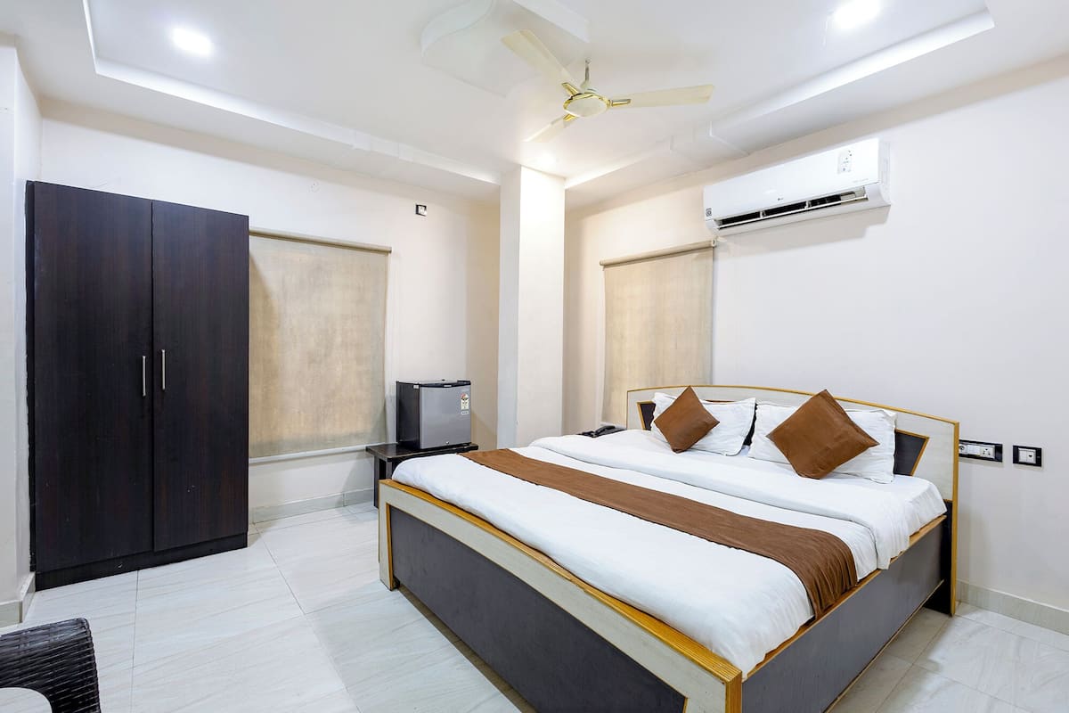 Una camera d'albergo con un letto, un armadio, una ventola a soffitto, un condizionatore d'aria e un piccolo tavolo.