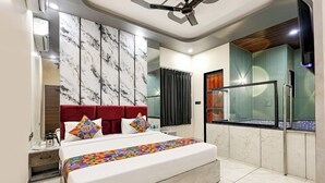 A modern bedroom with a marble-patterned wall, a red upholstered headboard, a large bed with colorful pillows, and a bathroom with a glass shower enclosure. - Fabhotel Prime Shyam Emprial (Khatoo)