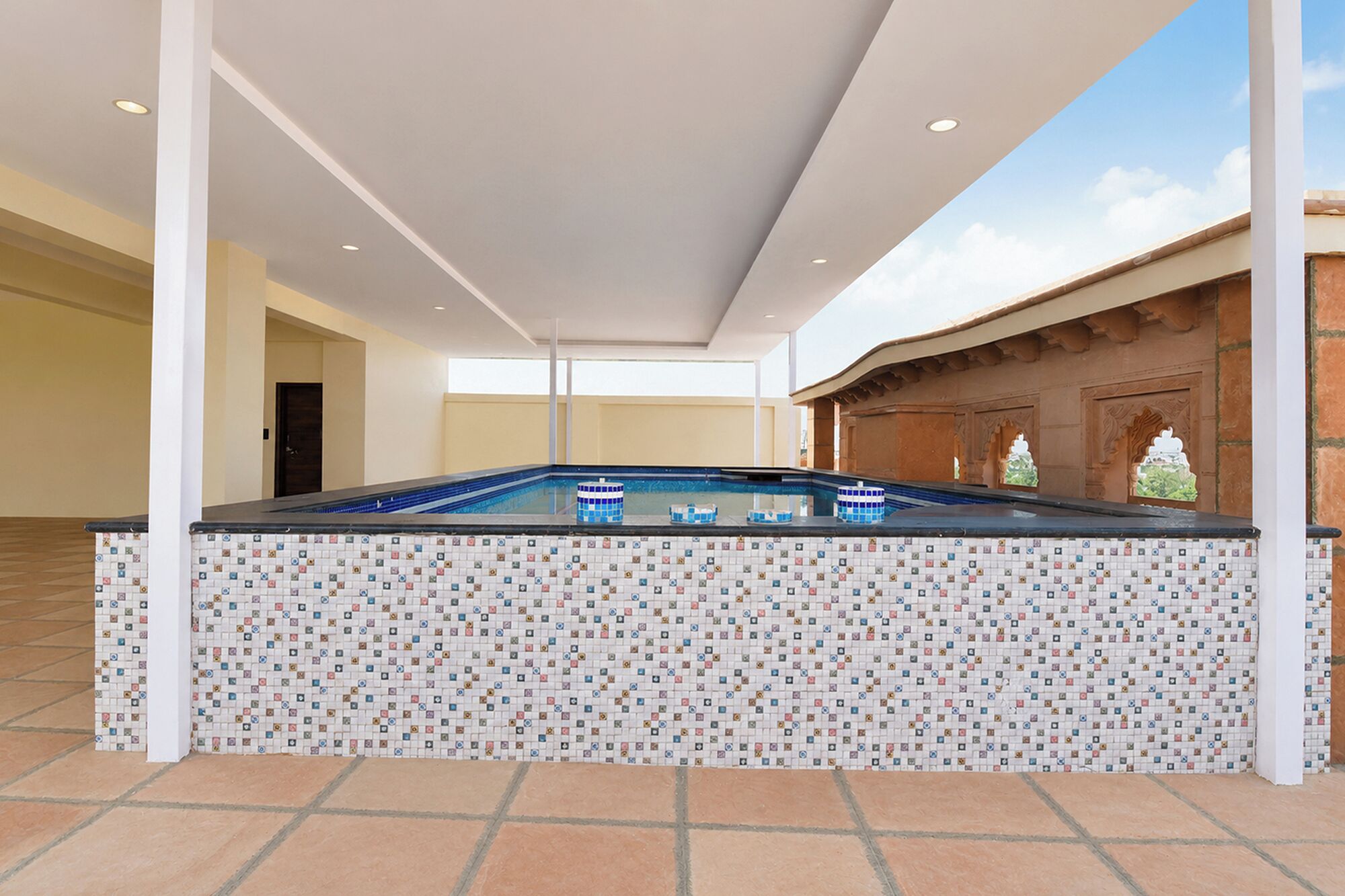 A pool area with a tiled floor, a pool with blue tiles, and a white ceiling.