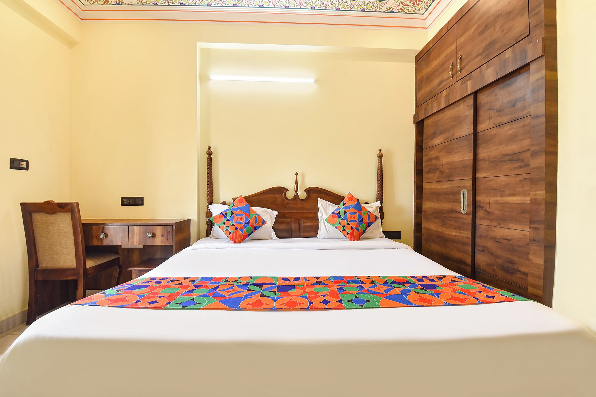 A hotel room with a bed, a wooden wardrobe, a nightstand, and a chair.