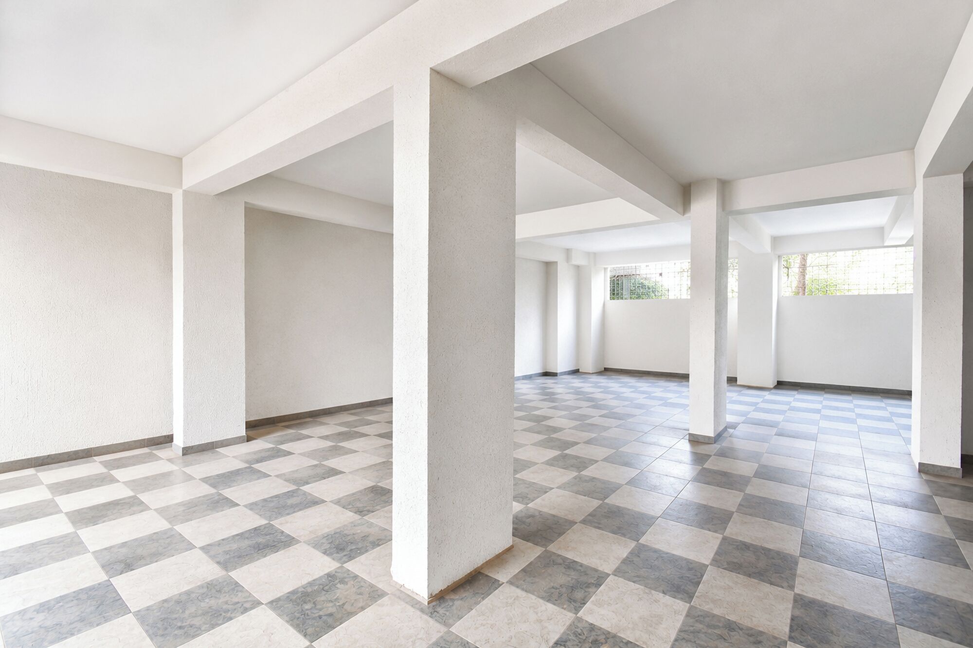 An empty room with a checkered floor, white walls, and large windows.