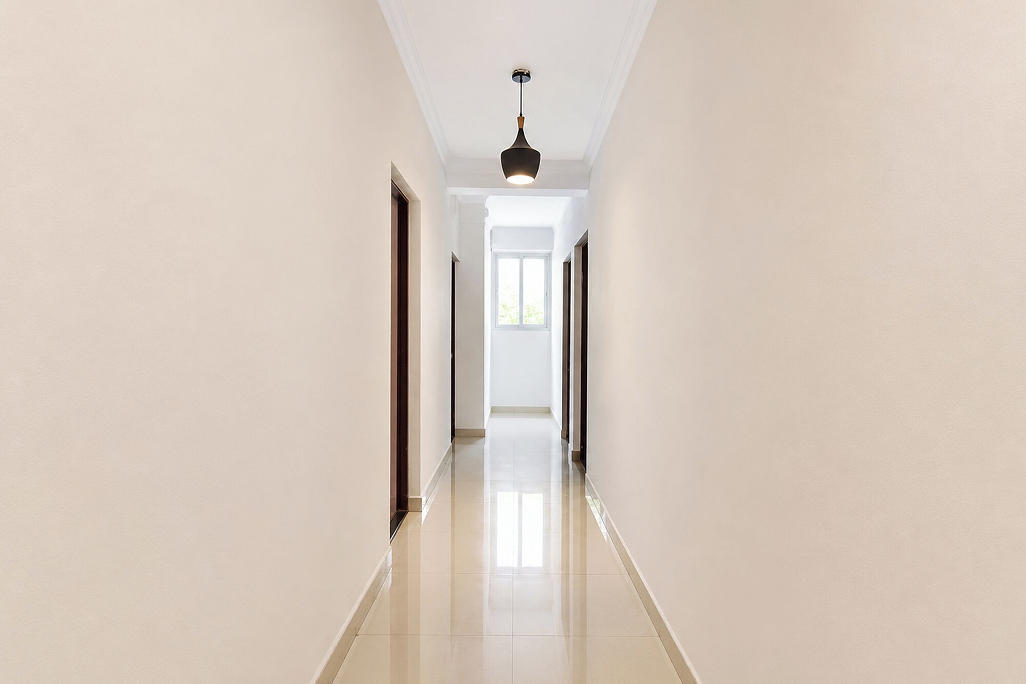 A long, narrow hallway with white walls and a shiny tiled floor, leading to a bright room with a window.