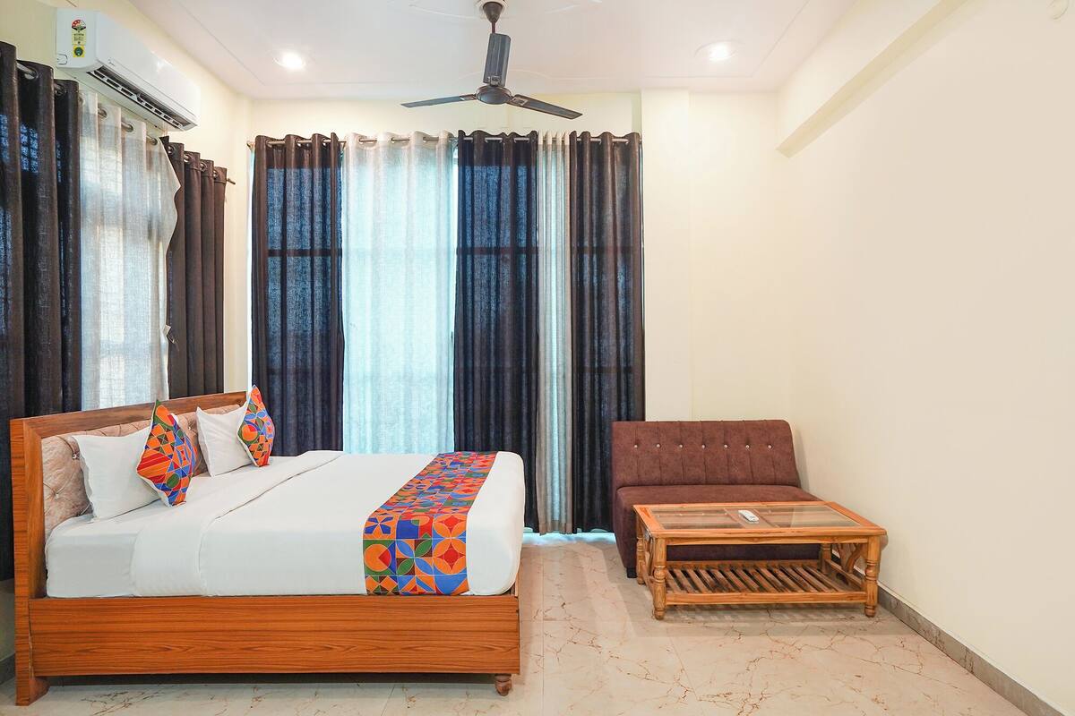 A bedroom with a bed, a wooden nightstand, a brown sofa, a ceiling fan, and a window with curtains.