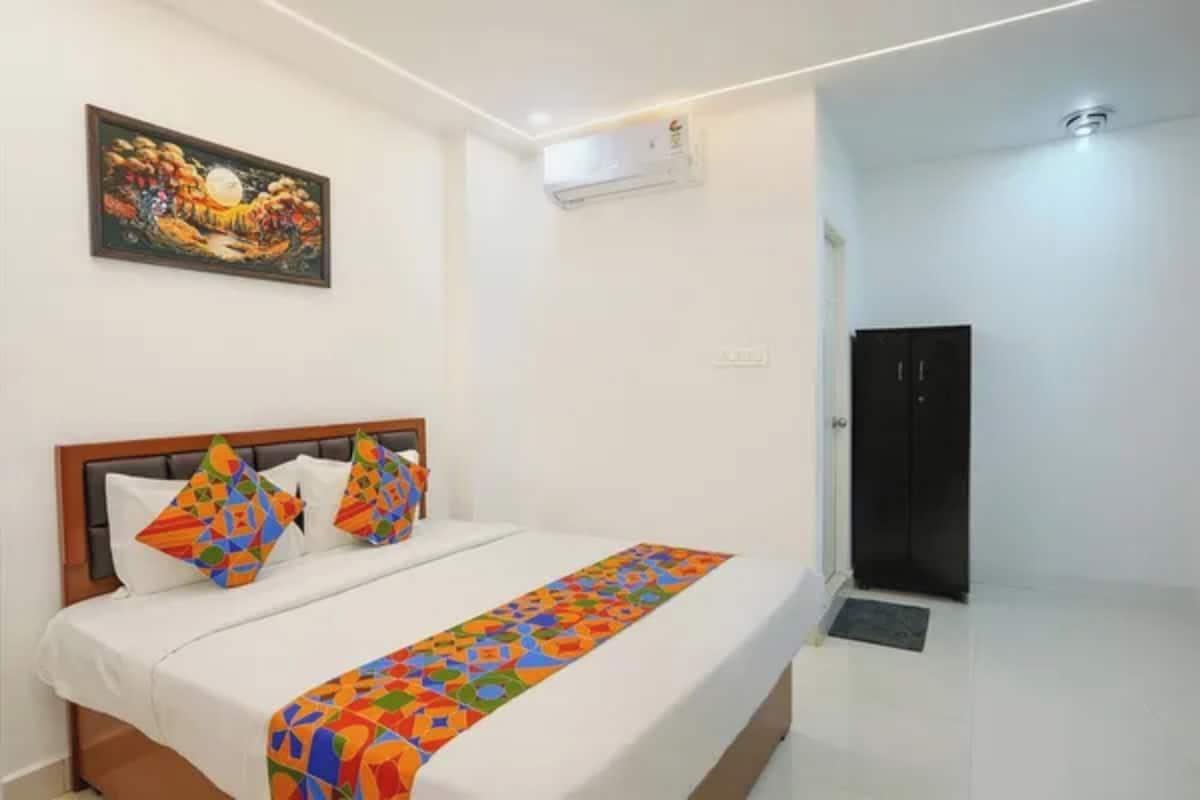 A hotel room with a bed, a colorful bedspread, a painting on the wall, and a black wardrobe.