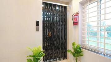 A door with a black metal gate, a fire extinguisher mounted on the wall, and two potted plants.