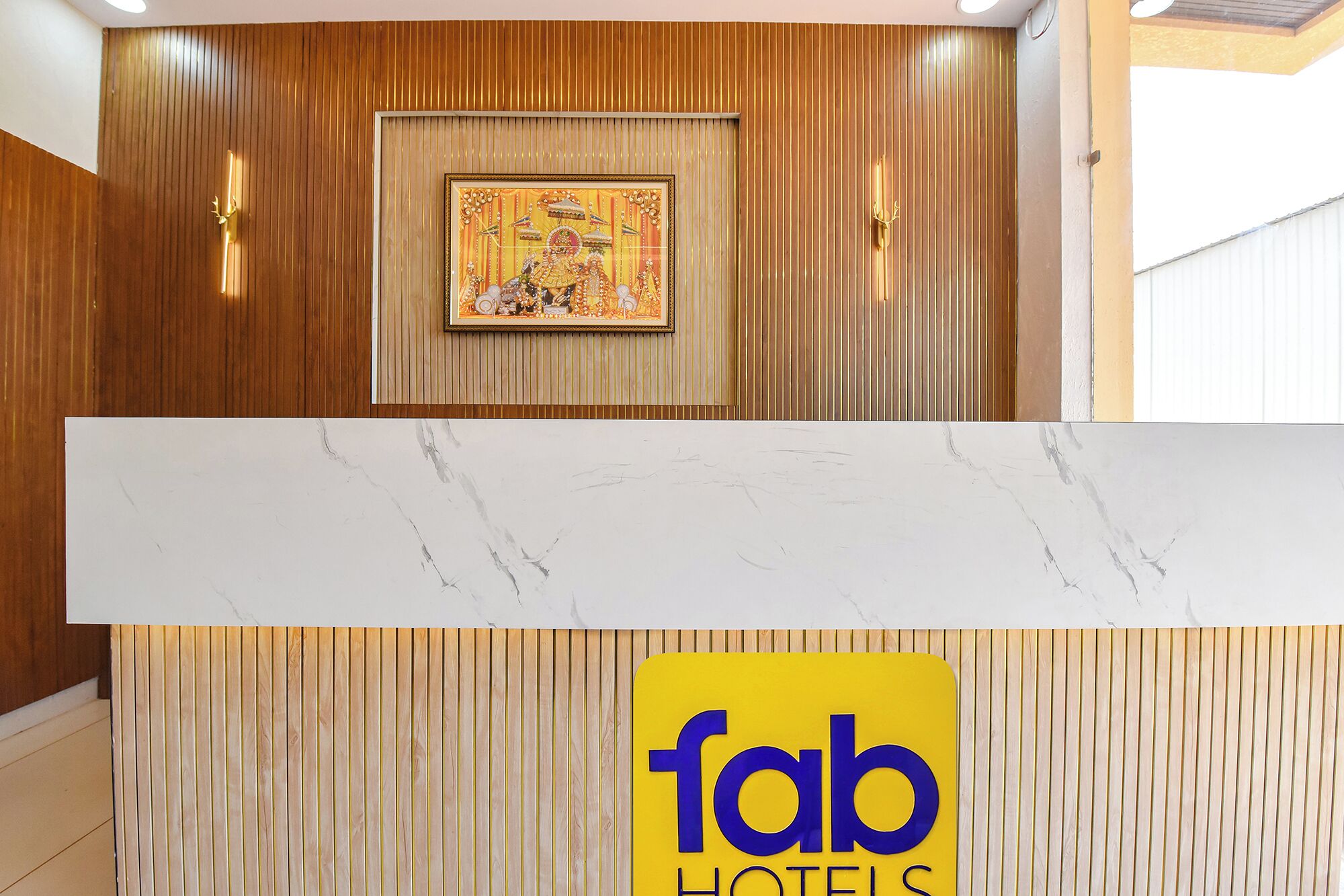 A hotel reception area with a wooden panel wall, a framed artwork, and a sign for Fab Hotels.