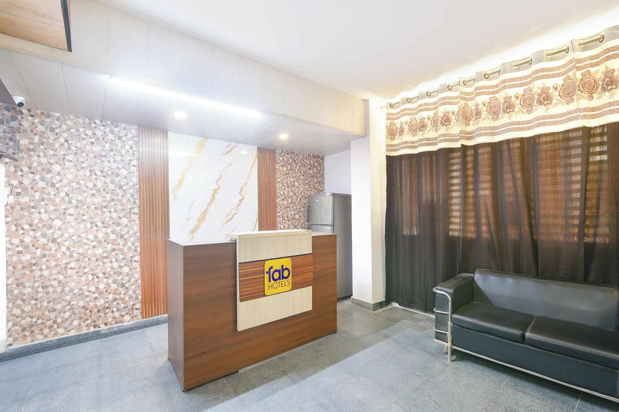 A hotel reception area with a wooden reception desk, a sofa, and a patterned wall.