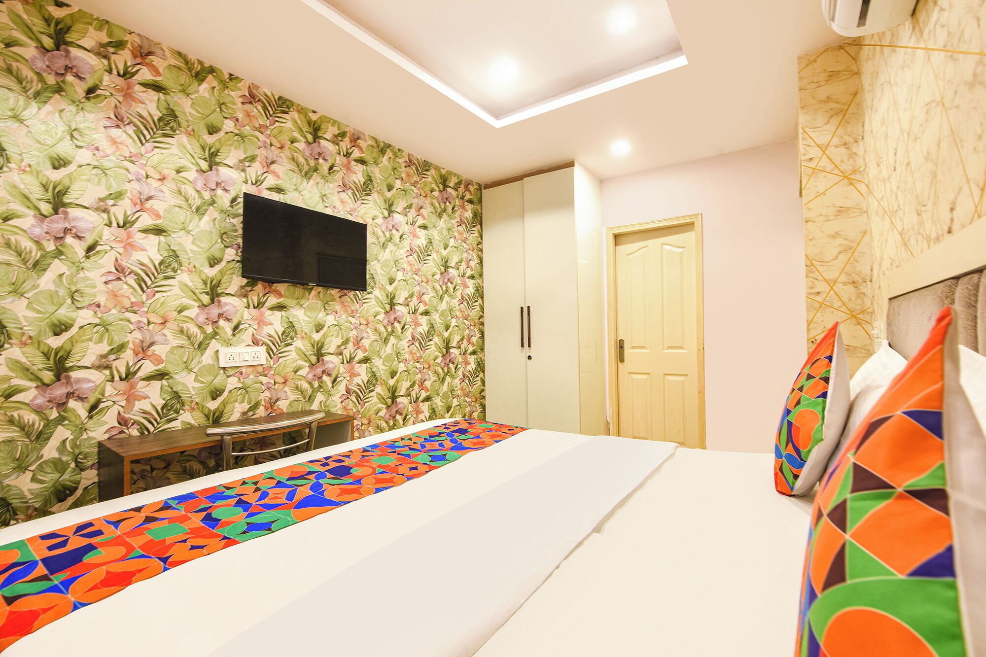A bedroom with a bed, a TV mounted on the wall, a wardrobe, and a door.