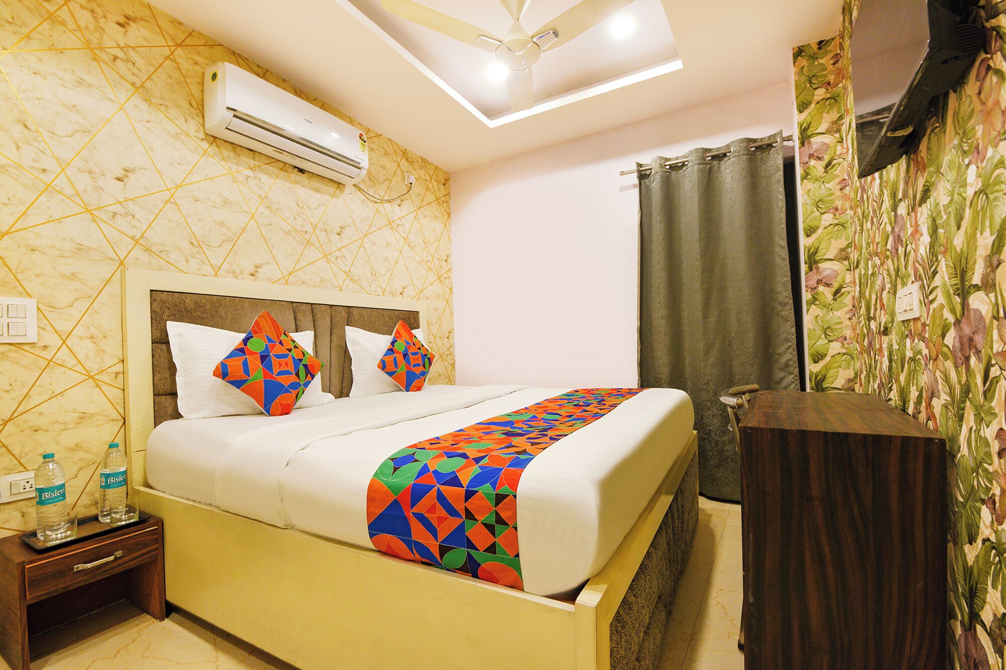 A hotel room with a bed, a nightstand, an air conditioning unit, a ceiling fan, and a shower curtain.