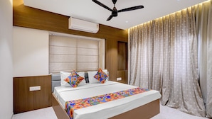 A bedroom with a bed, a ceiling fan, an air conditioning unit, a window with blinds, and a curtain.