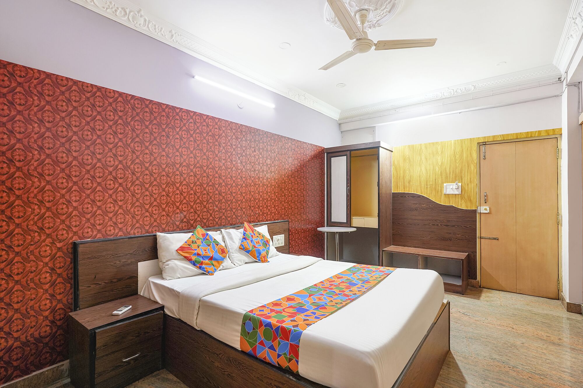 A hotel room with a bed, bedside tables, a wardrobe, a mirror, and a ceiling fan.