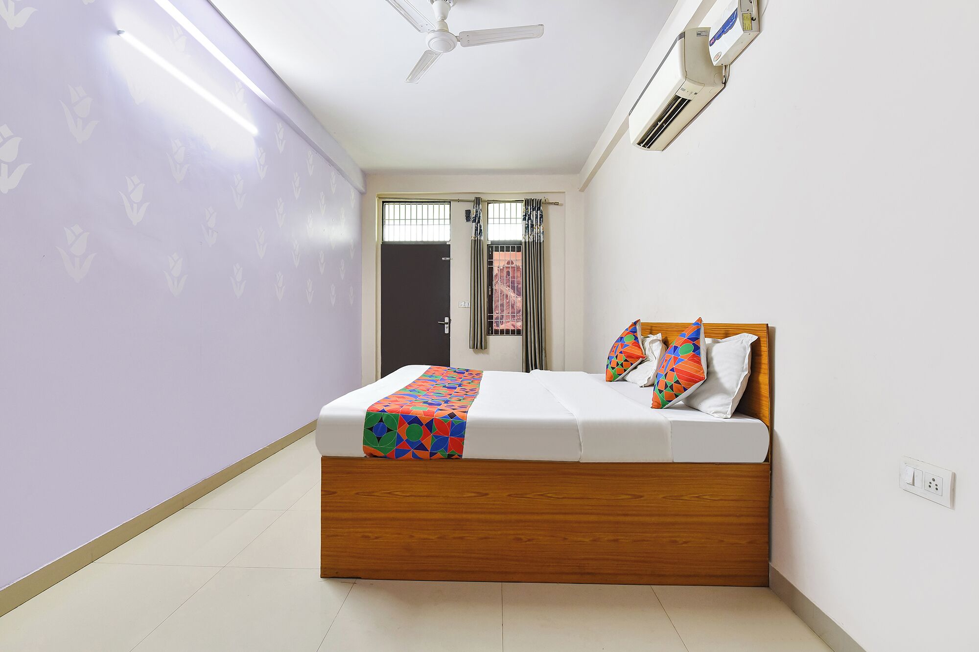 A bedroom with a bed, a ceiling fan, an air conditioner, and a window with curtains.