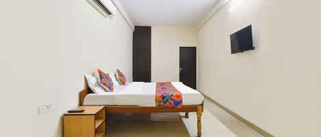 A bedroom with a bed, bedside table, air conditioning unit, ceiling fan, and a TV mounted on the wall.