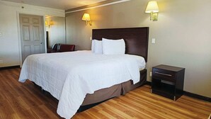 A hotel room with a large bed, a nightstand, two wall lamps, and a door.