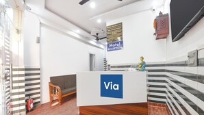 A hotel reception area with a Via sign, a Buddha statue, a reception desk, a fire extinguisher, and a check-in counter.