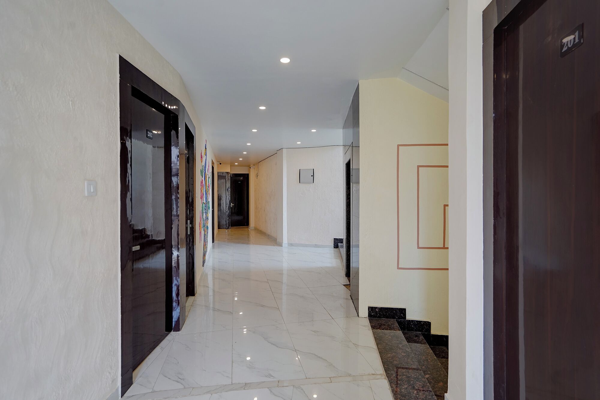 A hotel hallway with a marble floor, a dark door on the right, and a light-colored wall on the left.