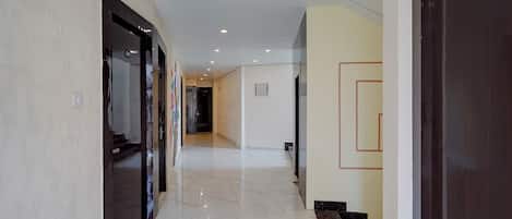 Un pasillo de hotel con piso de mármol, una puerta oscura a la derecha y una pared de color claro a la izquierda.