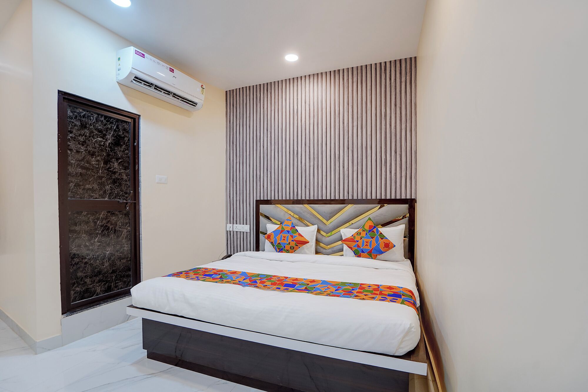 Un dormitorio con una cama, aire acondicionado instalado en la pared y una ventana con persianas verticales.