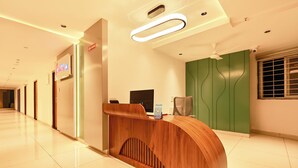 A hotel reception area with a wooden reception desk, a computer monitor, a QR code stand, and a green accent wall.
