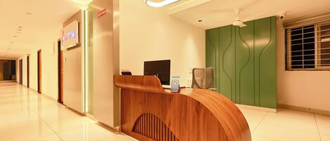 Zona de recepción de un hotel con un mostrador de madera, un monitor de ordenador, un soporte para código QR y una pared de acento verde.