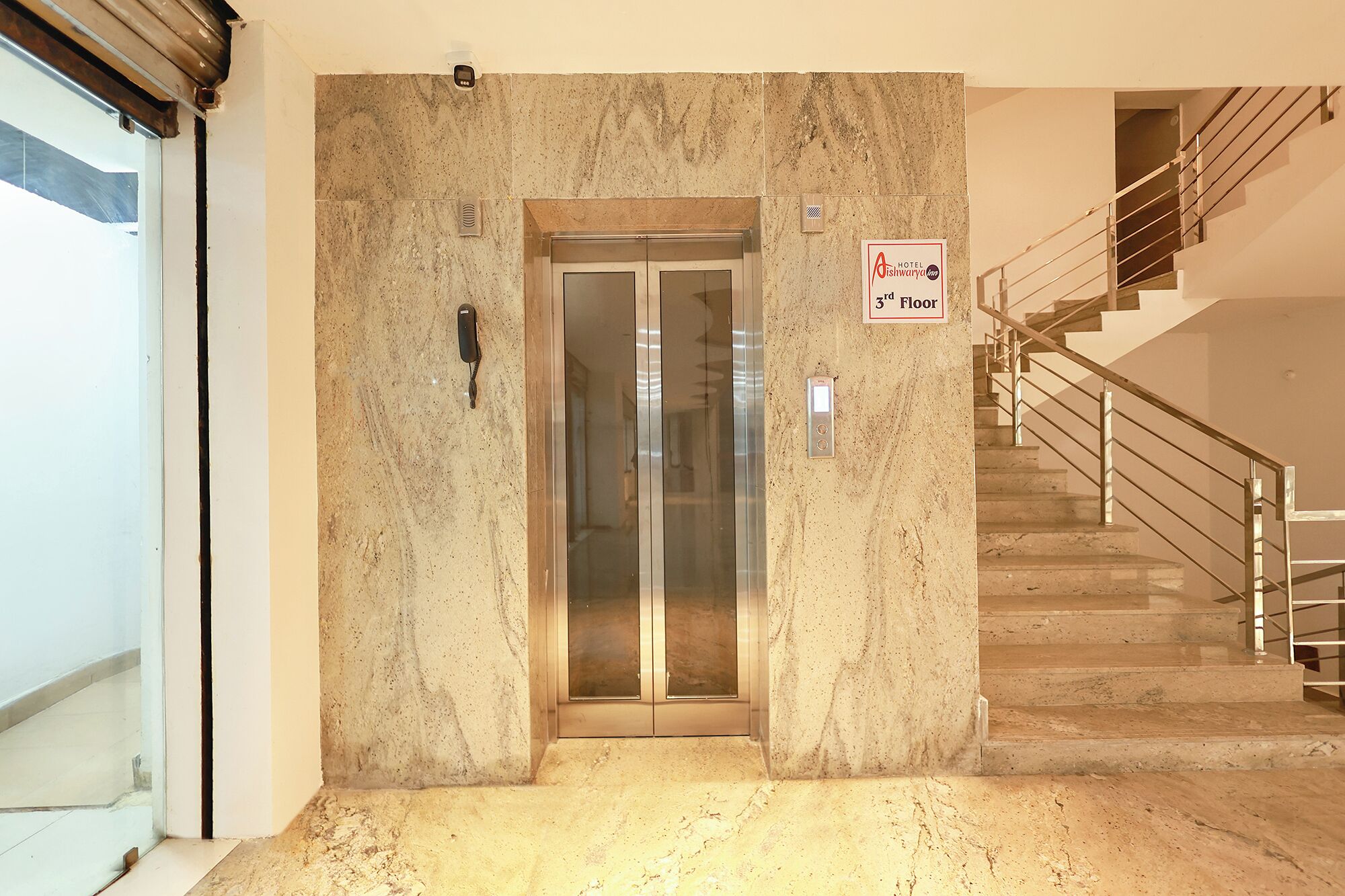 An elevator with a sign indicating the 3rd floor, a staircase with metal railings, and a wall with a textured surface.