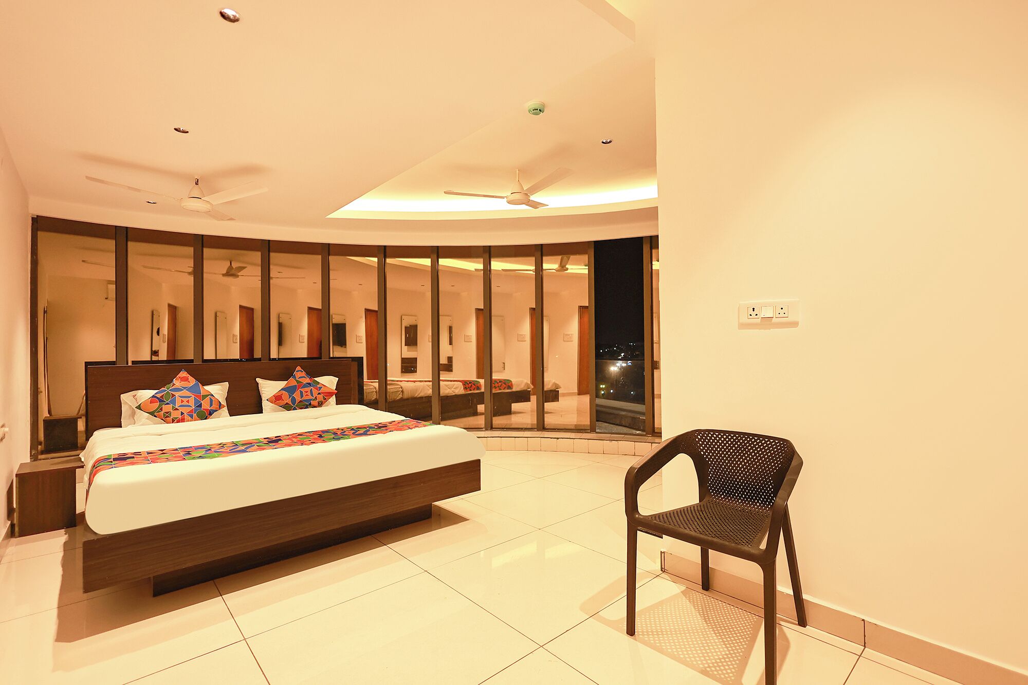 Habitación de hotel moderna con una cama grande, una silla y vistas a la ciudad de noche.