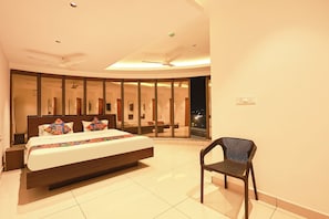 A modern hotel room with a large bed, a chair, and a view of the city at night. - FabHotel Aishwarya Inn (Hasanparti)