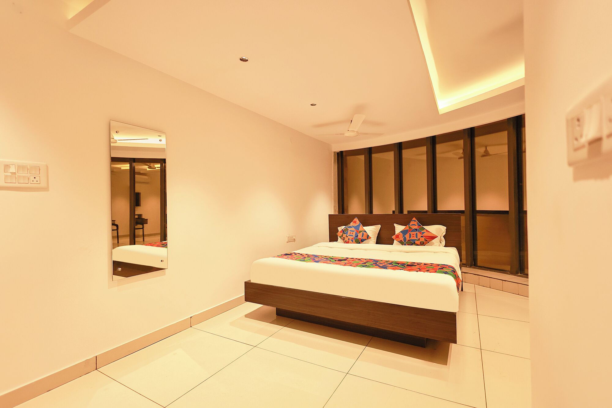 Quarto de hotel moderno com uma cama grande, um ventilador de teto, uma janela ampla e um espelho na parede.