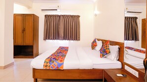 A hotel room with a bed, a wooden wardrobe, a bathroom mirror, and a bedside table with a phone and a scale.