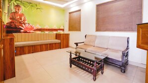 A modern living room with a sofa, a glass coffee table, a Buddha statue, and a ceiling fan.