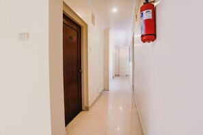A corridor with a fire extinguisher mounted on the wall, a wooden door, and a tiled floor. - FabHotel Ria Residency - Nr. Big Daddy Casino Cruise (Panaji)