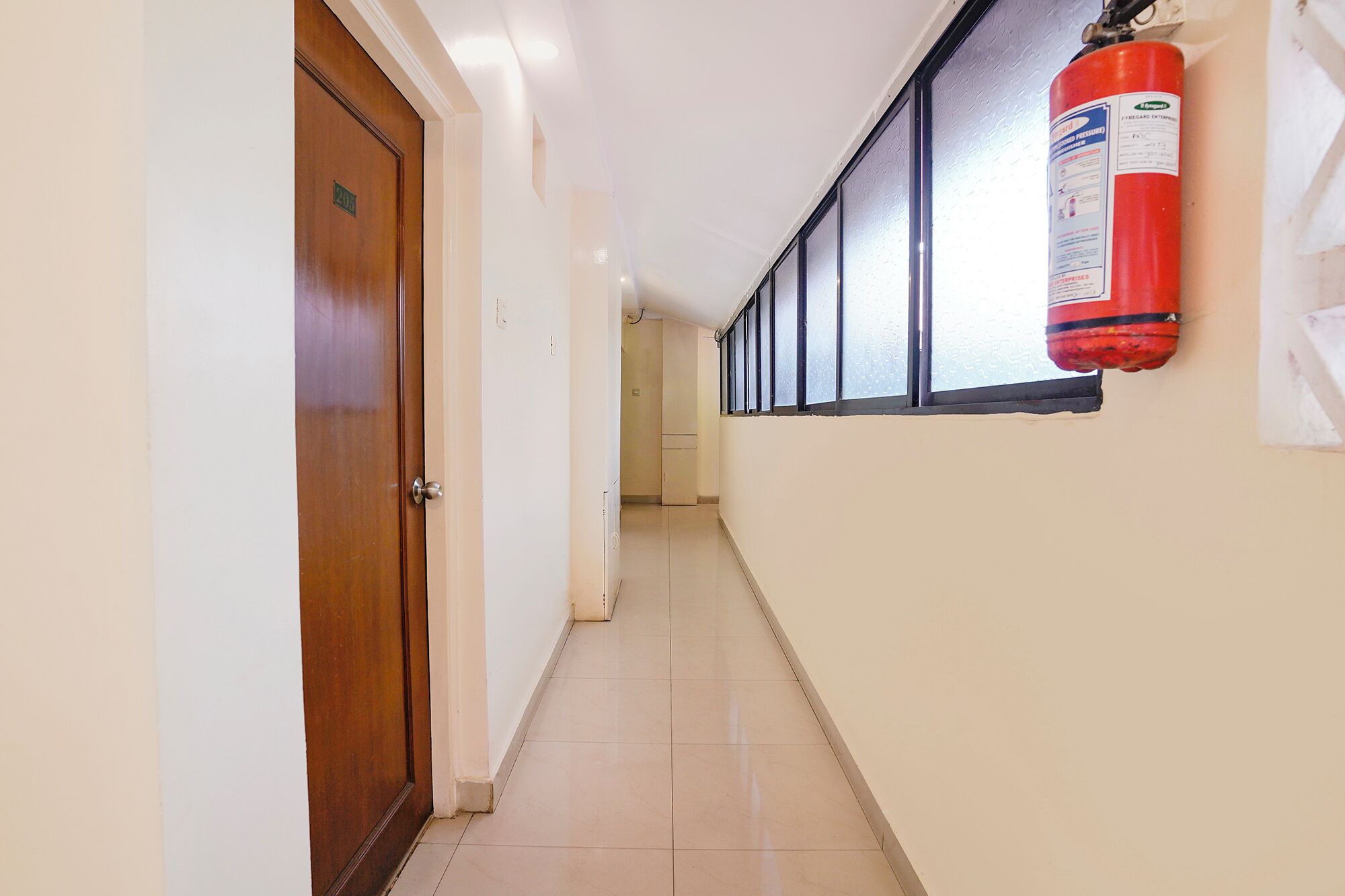 A hallway with a fire extinguisher mounted on the wall, a wooden door, and a tiled floor.