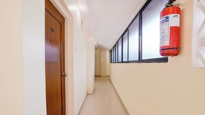 A hallway with a fire extinguisher mounted on the wall, a wooden door, and a tiled floor.