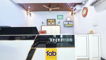 Een receptiebalie met een bordje 'fab hotels', een ingelijst beeld en een bordje 'SRI SAI RESIDENCY'.