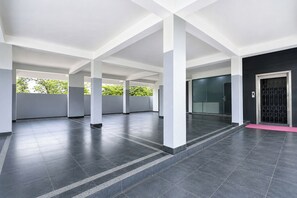 A spacious indoor area with a tiled floor, white pillars, and a glass door on the right. - Fabhotel Ssr (Khammam)