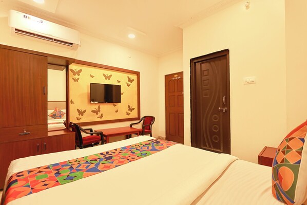 A hotel room with a bed, a TV mounted on the wall, a desk with a chair, and a door.