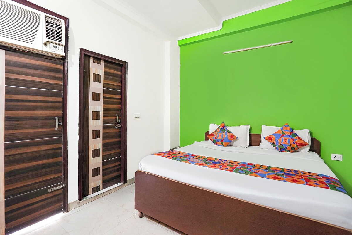 A bedroom with a bed, a green accent wall, a wooden wardrobe, and a window.