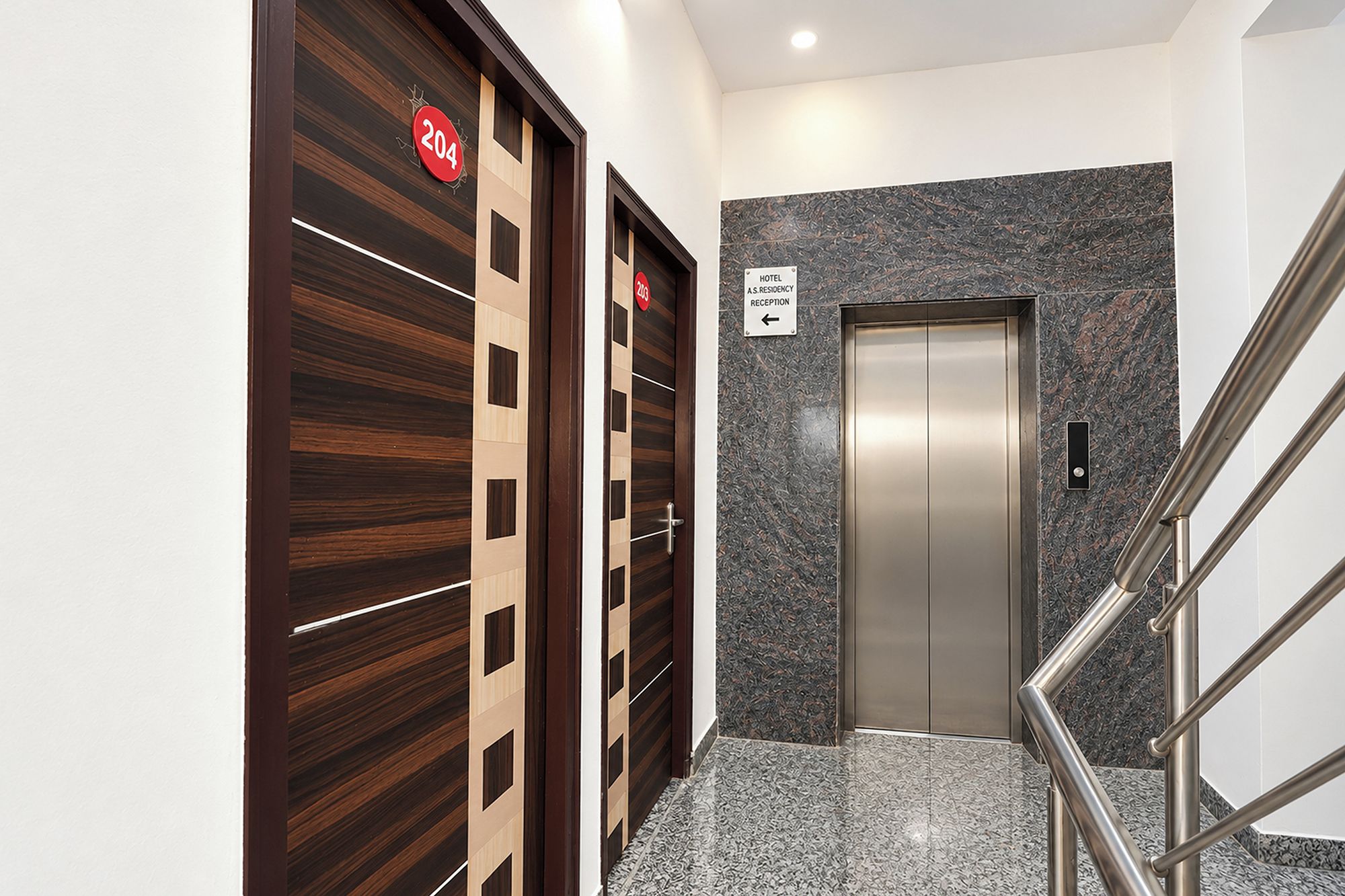 A hotel reception area with a reception desk, a sign indicating the direction to the reception, and an elevator.