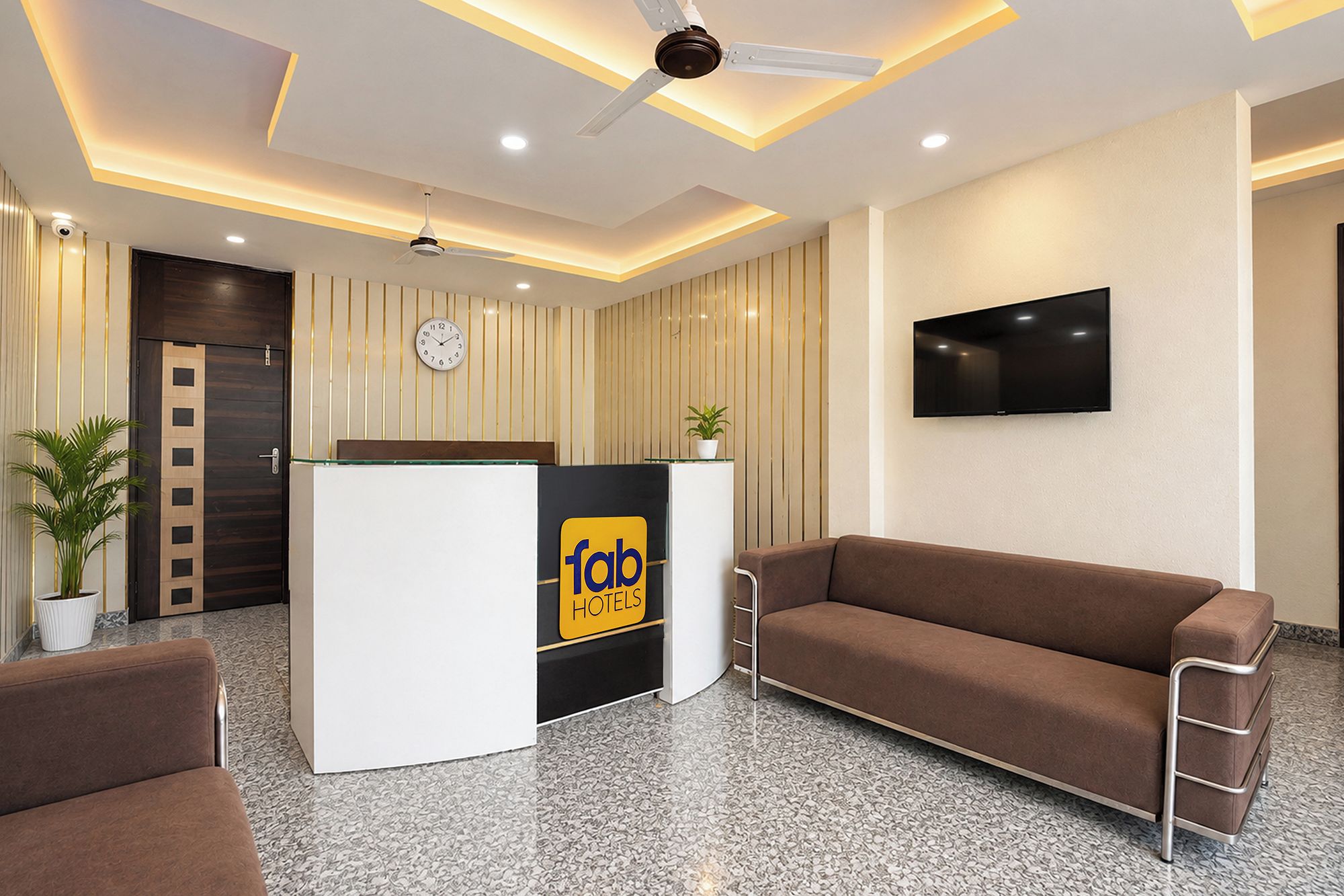 A hotel reception area with a reception desk, a clock, a television, and seating.
