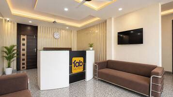 A hotel reception area with a reception desk, a clock, a television, and seating.