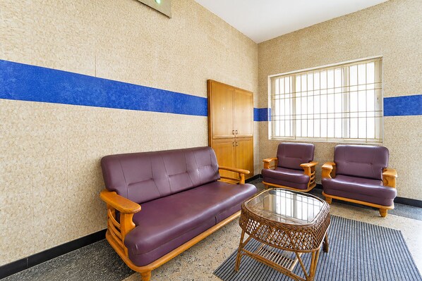 A room with a sofa, two armchairs, a glass-top table, a door, and a window with bars.