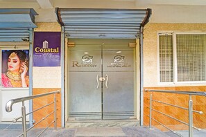 L’entrée d’un hôtel, fermée par un portail métallique, un panneau indiquant « Coastal Grand Hotels & Resorts », et une fenêtre à motifs géométriques.